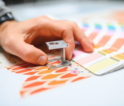 Why people choose our Printing Services - Quality Control. Print house worker controlling printing process quality and checking colors with magnifying glass.